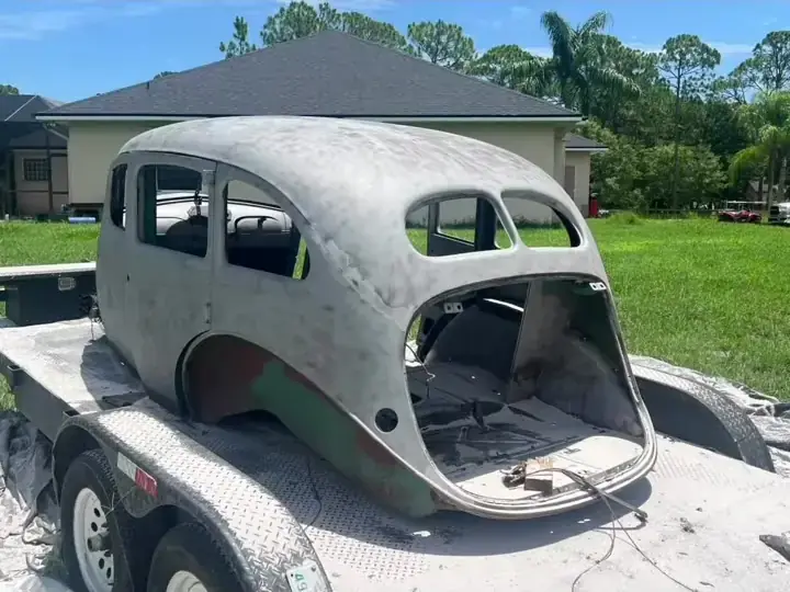 The same classic sedan body sandblasted to bare metal on a trailer