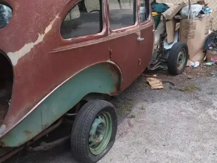 Rusted classic sedan body with faded green and brown paint before blasting