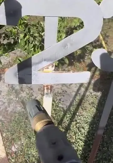Rusted steel sign numbers being sandblasted with the nozzle in view